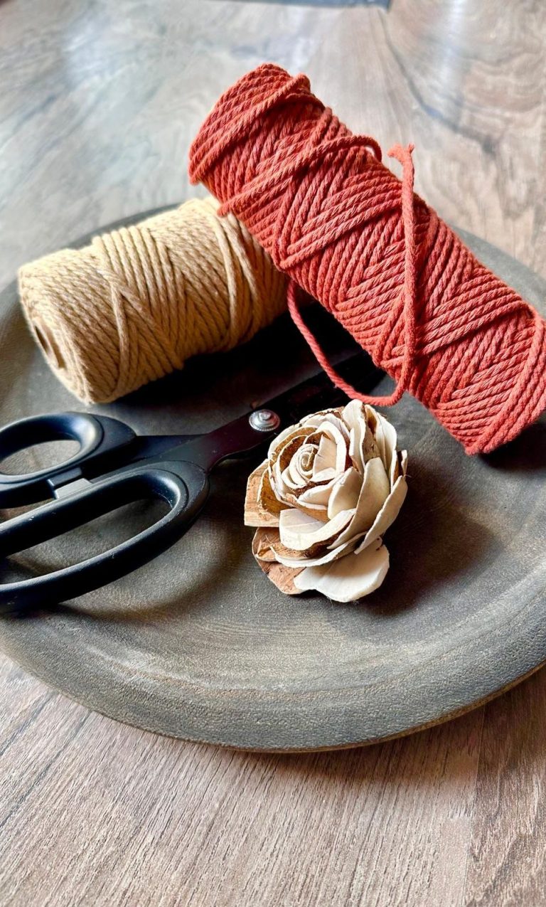 Bobines de fil rouge et beige, ciseaux et une fleur en bois sur une assiette en bois.