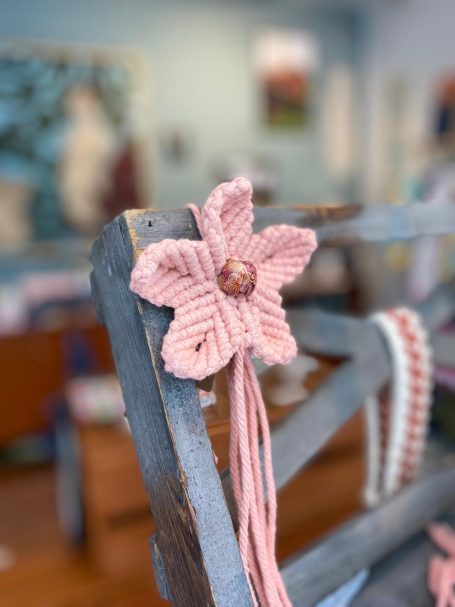 Fleur Fleur en macramé rose ornée d'un perle, accrochée à un support en bois.
